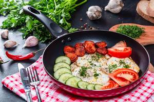 Fried eggs with vegetables and sausages in a frying pan with a knife and fork