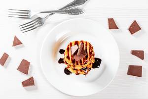 Fried pancakes with chocolate topping and pieces of chocolate on the table with forks