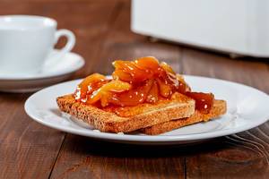 Fried Toast Slices with Peach Jam on a White Plate next to a White Cup of Tea for Breakfast on a Wooden Table