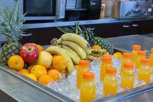 Frisch gepresster Fruchtsaft in Flaschen auf Eis, daneben Bananen, Äpfel, Ananas und Orangen