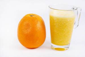 Frisch gepresster Orangensaft mit Fruchtfleisch in Glas neben ganzer ungeschälter Orange vor weiß