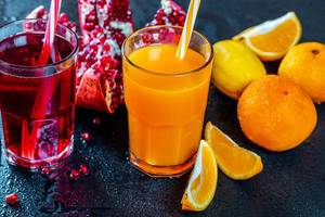 Frisch gepresster Zitrus-Orangensaft und ein Glas Granatapfelsaft mit Früchten auf schwarzem Hintergrund