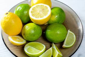 Frische Limonen, Limettenscheiben und halbierte Zitronen auf einem Glasteller
