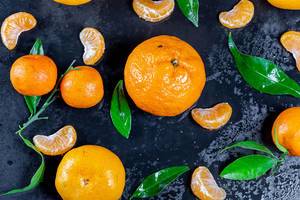 Frische Mandarinen mit Blättern und Stücken auf schwarzem Hintergrund