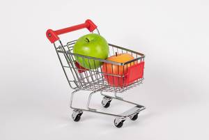 Frische, rote und grüne Äpfel liegen in Einkaufswagen vor weißem Hintergrund