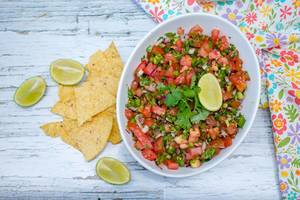 Frische Salsa in einer weißen Schale, neben Nachos und Limetten auf einem weißen Holztisch