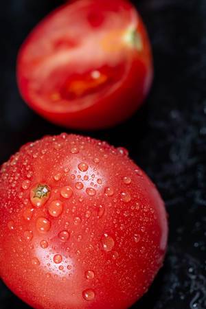 Frische Tomaten mit Wasser bestäubt auf schwarzem Hintergrund