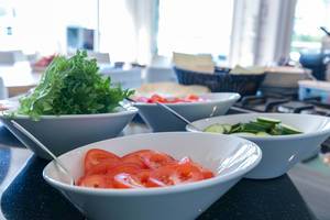 Frische Tomatenscheiben, geschnittene Gurken und grüne Salatblätter in weißen Schalen zum Frühstück auf der Büfetttheke im Hotel