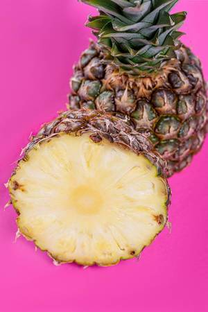 Frische und reife halbierte Ananas vor knallig pinken Hintergrund