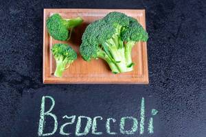 Frischer Broccoli mit Wassertropfen auf einem Küchenbrett und der Schrift Broccoli auf schwarzem Hintergrund
