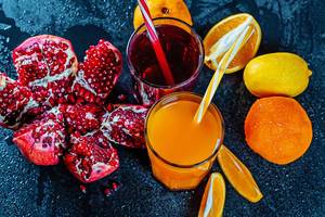 Frischer Fruchtsaft aus Orangen und Granatäpfeln mit reifen Früchten auf schwarzem Hintergrund in der Aufsicht