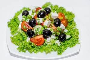 Frischer griechischer Salat bestehend aus grünen Blättern, schwarzen Oliven, Tomaten und Fetakäse