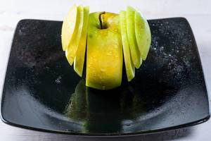 Frischer, grüner Apfel in Scheiben geschnitten auf einem schwarzen Teller mit Reflektion