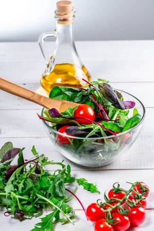 Frischer Salat-Mix mit Rucola, Spinatblätter, Tomatenstaude und Olivenöl auf einem weißen Holztisch