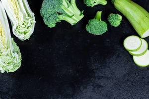 Frisches Gemüse, Kohl, Zucchini und Broccoli mit Wassertropfen auf schwarzem Hintergrund