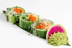 Frisches Sushi mit Gurke, Avocado, Krabbenfleisch, Rucolasalat und Microgreens, auf einem langen grünen Blatt neben Wasabi-Sauce angerichtet