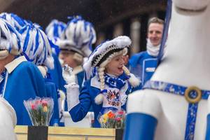 Fröhliche Frau im traditionellen blau-weißen Kostüm der Blauen Funken wirft Kamellen (Süßwaren) beim Rosenmontagsumzug in Köln