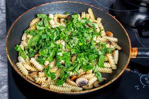 Frying pan with pasta, mushrooms and herbs on the electronic hob