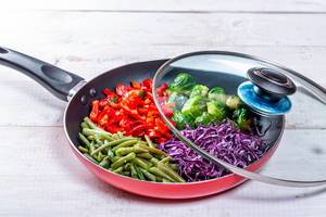 Frying pan with sliced vegetables on white wooden table