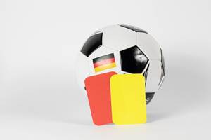 Fußball mit gelber und roter Schiedsrichterkarte vor weißem Hintergrund
