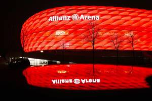 Fußballstadion in München: rot-beleuchtete Allianz Arena mit Spiegelung