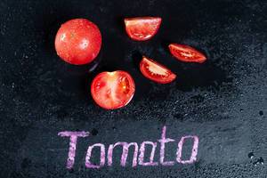 Ganze Tomaten und Tomatenstücke auf schwarzem feuchtem Hintergrund mit der Schrift Tomato