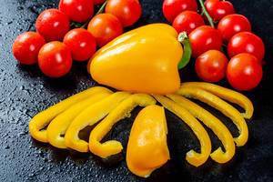 Ganze und in Streifen geschnittene gelbe Paprika mit Tomatensträuchern auf schwarzem Hintergrund