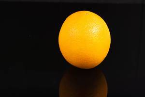 Ganze ungeschälte Orange freigestellt vor schwarzem Hintergrund mit Spiegelung