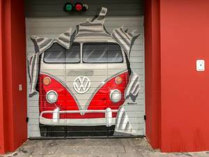 Garagentor bemalt als würde ein alter roter VW-Bus T1 durch das Tor fahren