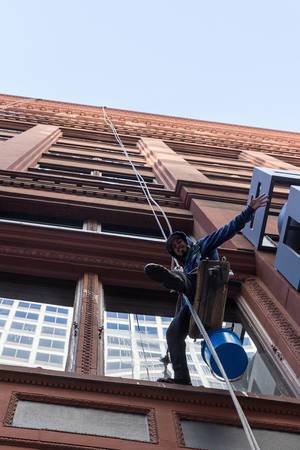 Gebäudereiniger grüßt den Fotografen während der Arbeit am Seil ohne Gerüst