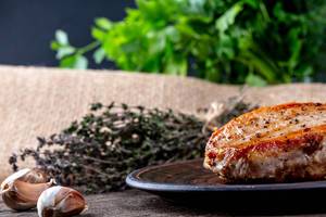 Gebratenes Fleisch auf braunem Teller mit Knoblauch und Kräutern auf einem Holztisch