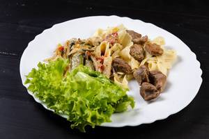 Gebratenes Gemüse mit Nudeln und Schweinefleisch, mit Salat auf einem Teller angerichtet auf schwarzem Holztisch