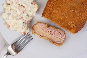 Gefülltes Schweinefleisch mit Käsefüllung und Gemüsesalat, als deftiges Mittagessen, auf einem weißen Teller