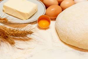 Gekneteter, rund geformter Teig drapiert mit Ingredienzen wie Eiern, Mehl, Butter und Weizenähren