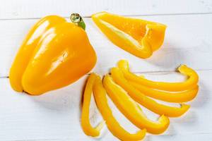 Gelbe Paprika, ganz und in dünne Streifen geschnitten, auf weißem Holztisch