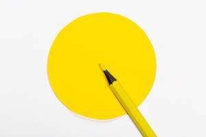 Gelber Holzmalstift zeigt in einen gelben Kreismittelpunkt als Symbol für Präzision