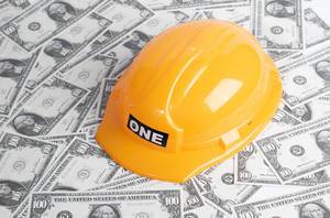 Gelber Schutzhelm für Bauarbeiter auf verteilten Banknoten symbolisiert Bauindustrie
