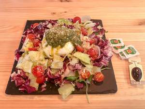 Gemischter Salat mit Kirschtomaten, Mozzarella, Pesto und geriebenem Parmesan Käse auf einer schwarzen Schieferplatte