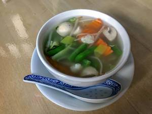 Gemüsesuppe mit frischem Gemüse und blauem Reislöffel aus Porzellan
