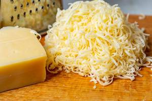 Geriebener Käse mit einem Stück Käse und einer Reibe auf einem Brett