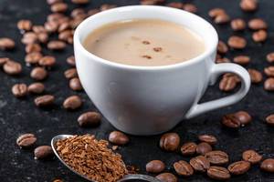 Geröstete Kaffeebohnen und heißer Kaffee in einer weißen Tasse auf dunklem Untergrund