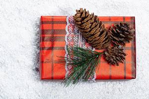 Geschenkbox für das neue Jahr - dekoriert mit Weihnachtsbaum- Ästen und -Zapfen vor dem Hintergrund von Schnee