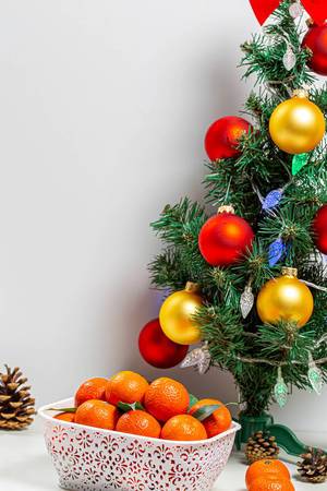 Geschmückter Weihnachtsbaum mit einer Schachtel reifer Mandarinen und einigen Zapfen