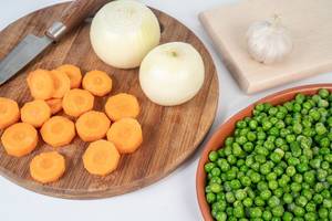Geschnittene Karottenscheiben, ganze Zwiebeln und grüne, tiefgekühlte Erbsen