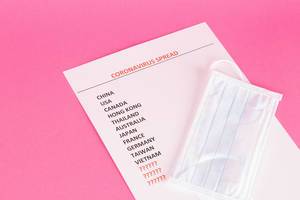 Gesichtsmaske liegt auf Liste mit Coronavirus betroffenen Ländern auf pinkem Hintergrund