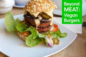 Gesunder Burger von Beyond Meat Burger, für eine vegane Ernährung, angerichtet im Burgerbrötchen, mit Sauce, Salat, Gurken, Tomaten und Zwiebeln
