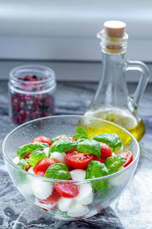 Gesunder Caprese-Salat, mit halben Tomatenstücken, ganzen Basilikum-Blätter, Mozzarella und Olivenöl in einer Karaffe