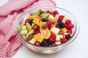 Gesunder Obstsalat mit Apfel, Himbeeren, Mandarinen, Trauben und Maulbeeren in einer Glasschüssel