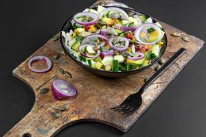 Gesunder Salat mit Gurken, Sonnenblumenkernen, Zwiebeln und Avocado in einer schwarzen Schale mit Gabel auf einem Holzschneidebrett