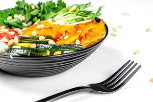 Gesunder Salat mit Kiwano Horngurke, Pinienkernen, Avocado-Scheiben, Mikrogrün, Petersilie und frischem Salat in einer schwarzen Schale mit schwarzer Gabel